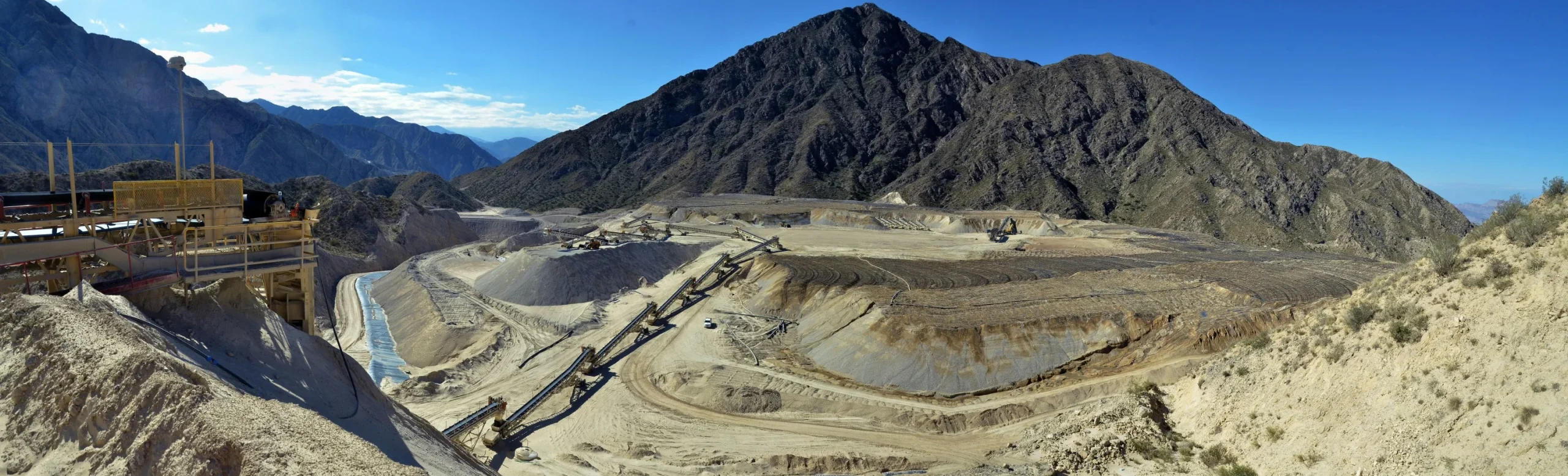Paisaje de la operación minera en Mina Gualcamayo con maquinaria pesada y terreno montañoso.