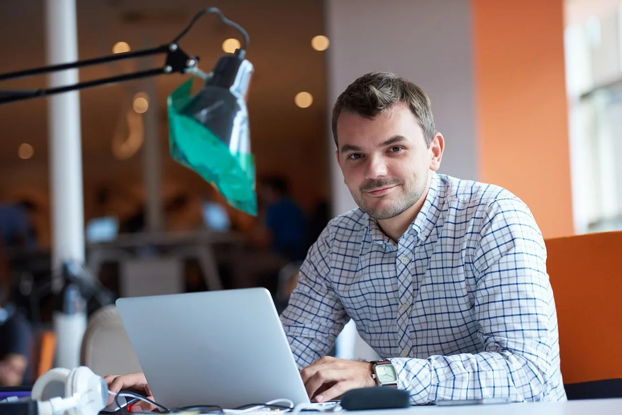 Un joven profesional trabajando con laptop en una oficina moderna.