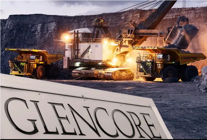 Logotipo de Glencore y vista de una de sus operaciones mineras, como una fundición o un puerto de carga.