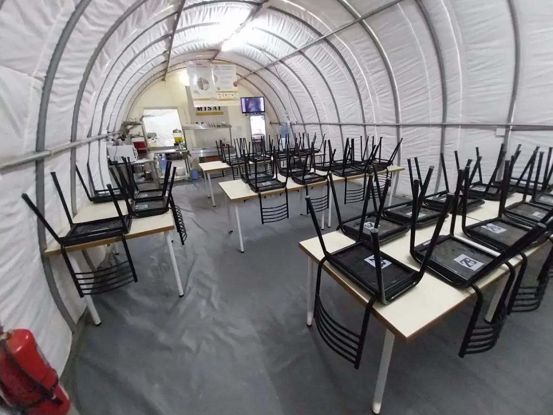  Interior de un amplio comedor en campamento minero, con mesas y sillas preparadas para el servicio de comidas.