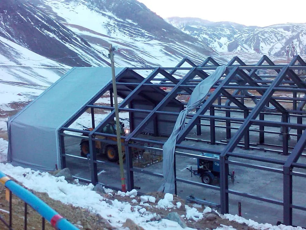 Gran carpa estructural de lona blanca instalada en un predio industrial, usada como taller minero.