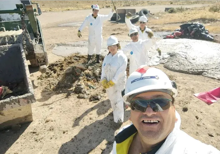  Grupo de trabajadores mineros, incluyendo a Yamila Montiel, posando sonrientes en el área de gestión de residuos de la mina.