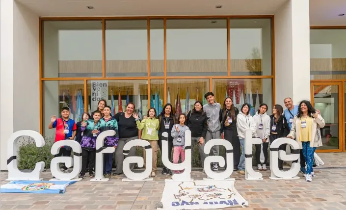 Grupo de jóvenes estudiantes observando y participando en actividades científicas en una feria escolar.