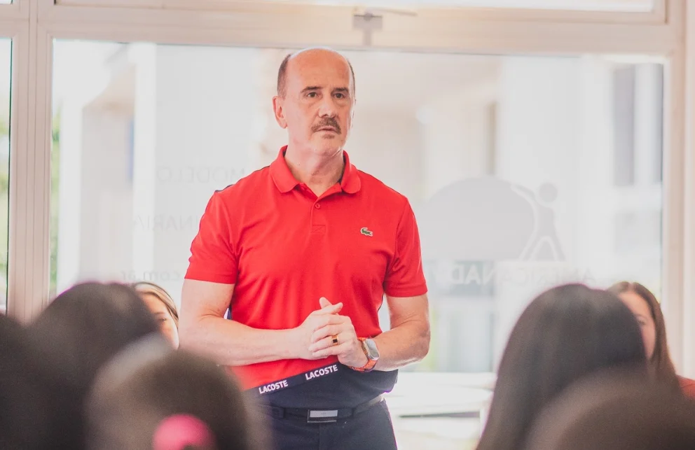 Retrato de Ernesto González, hombre sonriente en camisa, frente a un edificio con el logo de American Advisor.
