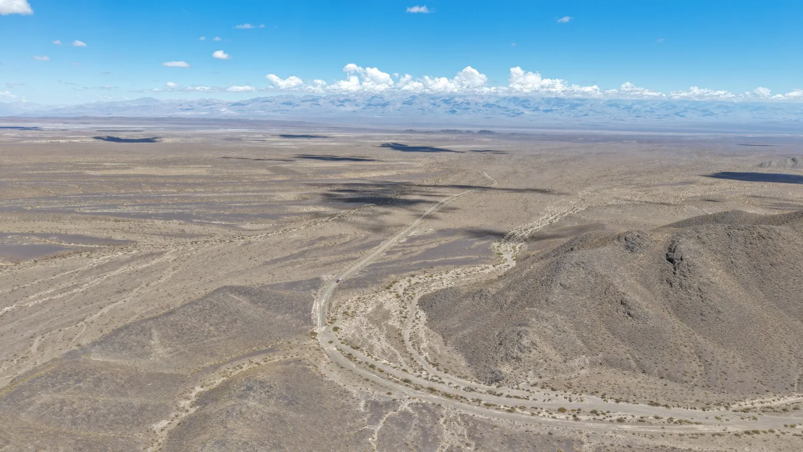 Camino de tierra con curvas que serpentea por un terreno árido y montañoso, bajo un cielo despejado.