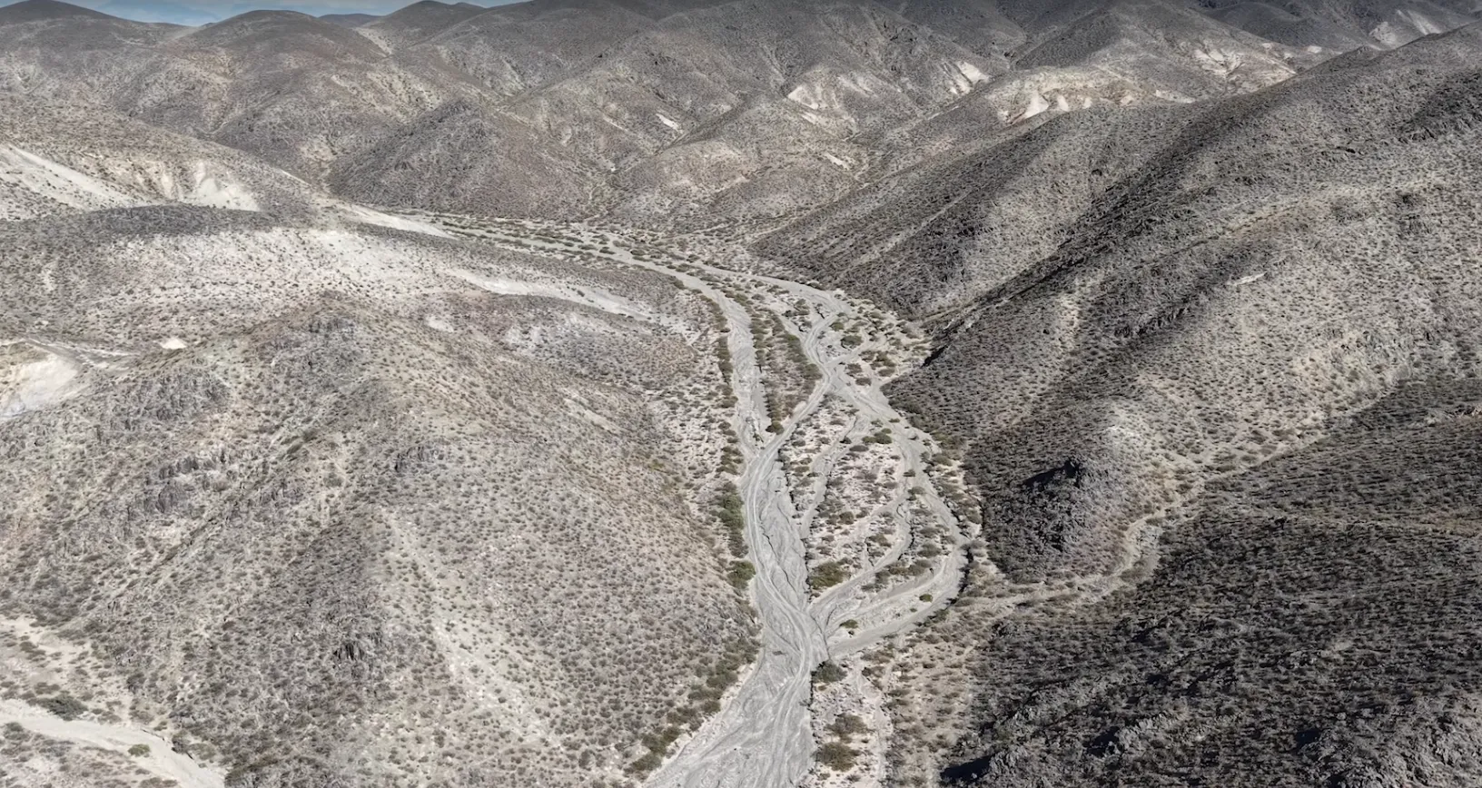Camino de tierra serpenteante a través de un paisaje árido montañosas, bajo un cielo claro.