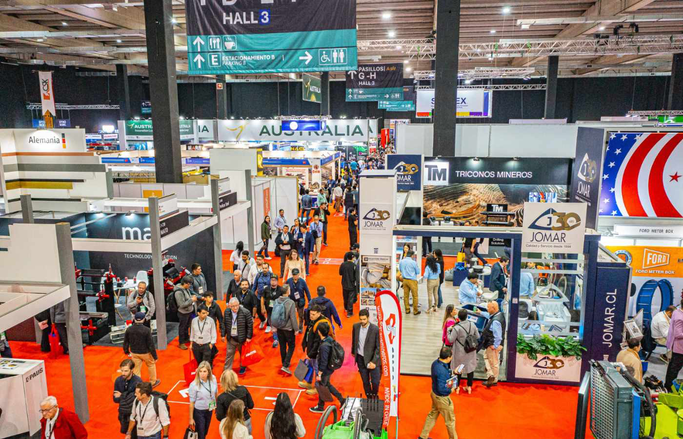 Profesionales, inversores y visitantes recorriendo los pasillos de una exposición minera con stands de empresas operadoras y proveedores industriales.