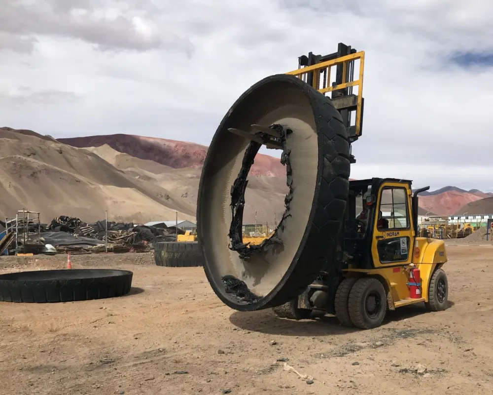Autoelevador amarillo Indram transportando una sección cortada de la banda de rodadura de un neumático minero gigante en la cordillera.