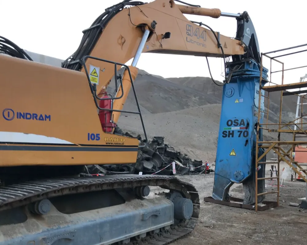 Excavadora Liebherr amarilla de Indram equipada con una cizalla hidráulica azul marca OSA para el corte de neumáticos mineros gigantes.