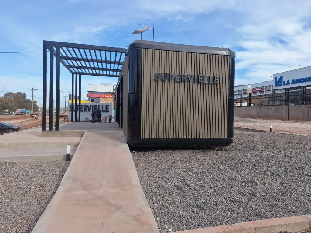 Edificio modular de color oscuro con el cartel "SUPERVIELLE", con escalinatas de cemento y un diseño institucional robusto.