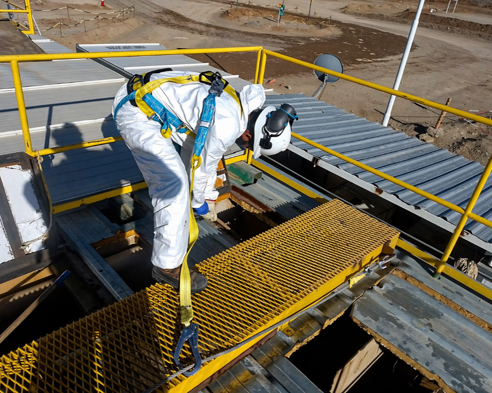 Técnico con traje de protección y arnés de seguridad inspeccionando infraestructura en planta de tratamiento de agua para minería.