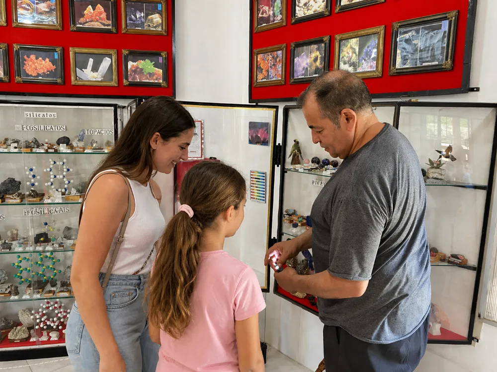 Osvaldo Merenda, con un mineral en la mano, explica sus características a un niño curioso y a su familia. El grupo está frente a una vitrina de exhibición.