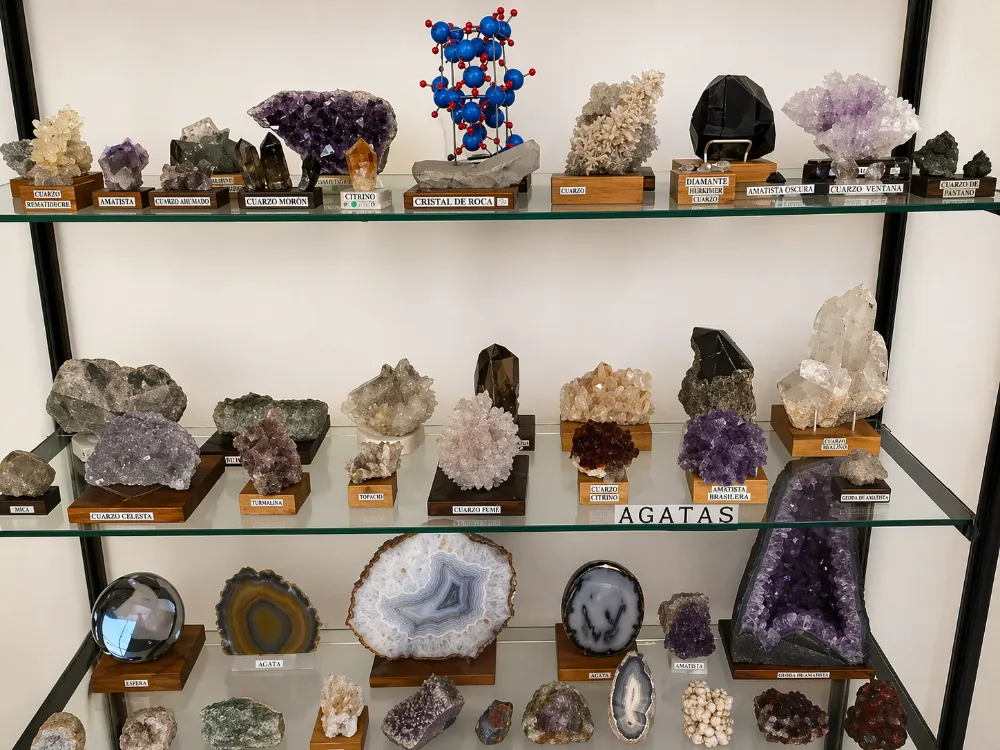 Primer plano de una estantería de exhibición en el Museo Piedras del Mundo, mostrando una colección diversa de minerales, cristales geométricos y gemas talladas.