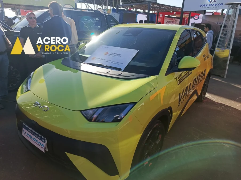 Auto pequeño color amarillo, eléctrico, con líneas modernas. Se muestra sobre una plataforma giratoria dentro de un stand minero.