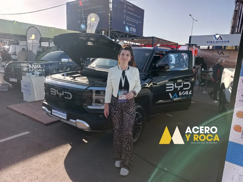 Karen Rubia de pie frente a una camioneta pickup gris BYD Shark. Al fondo se ven stands de la feria minera.