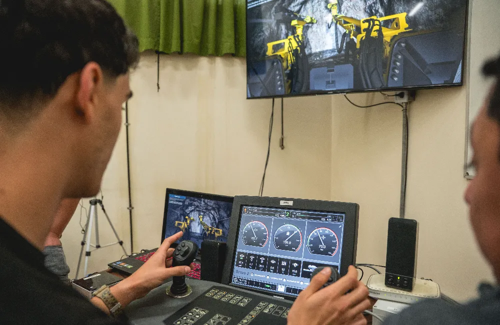 Vista en perspectiva de un operario frente a una estación de trabajo con múltiples monitores que proyectan el entorno 3D de una galería de mina subterránea.
