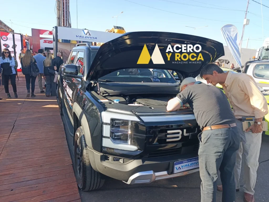 Grupo de personas con acreditaciones de la feria, inclinadas sobre el vano motor abierto de una camioneta. Se ven cables naranjas (alta tensión) y el motor térmico.