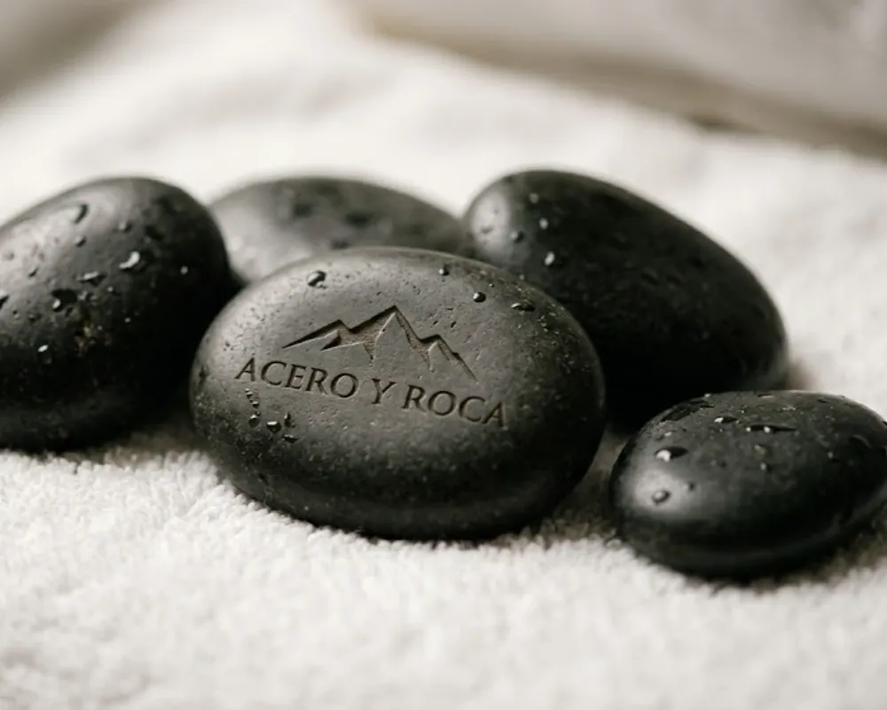 Primer plano de rocas volcánicas de basalto lisas y oscuras sobre una toalla blanca en un entorno de spa profesional. Contenido Original de ACERO Y ROCA - Prohibida su reproducción