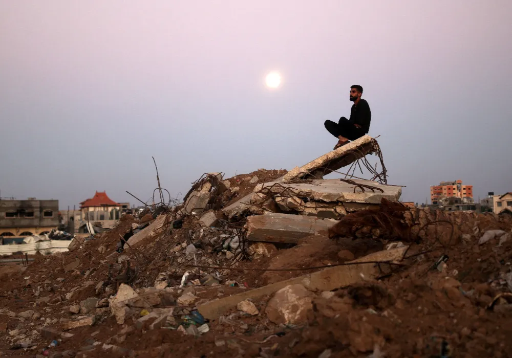 Un hombre sentado sobre una montaña de escombros, con la luna alzándose de fondo. Eyad Baba -AFP Getty Images.