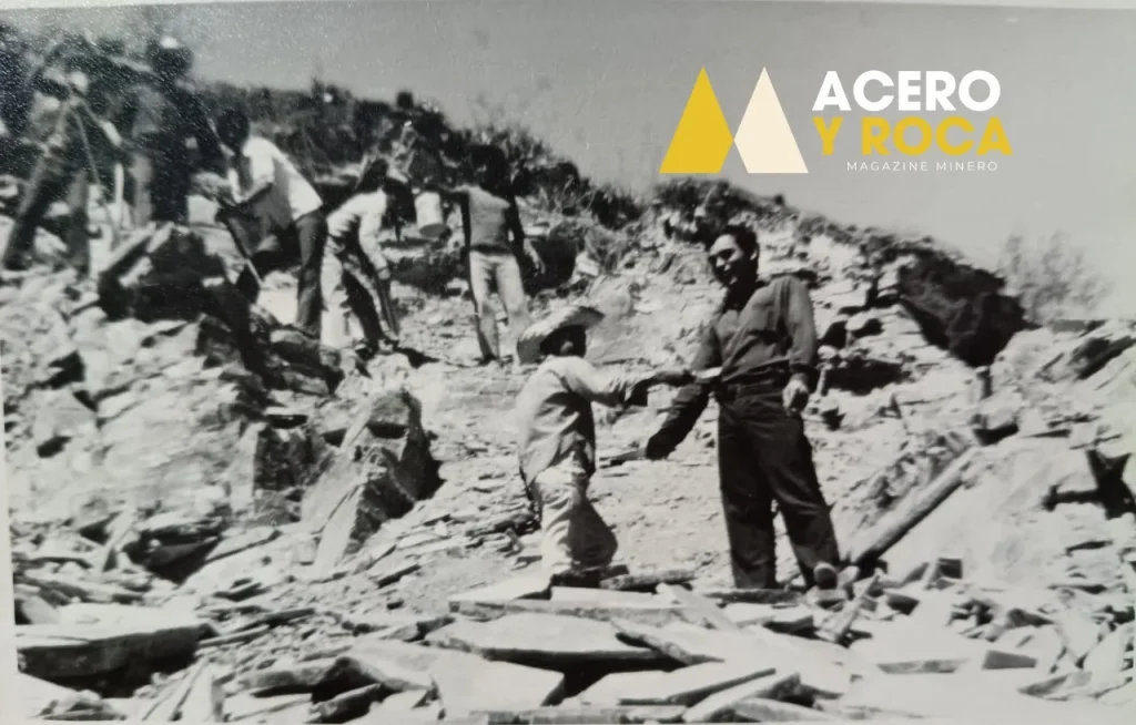 Fotografía histórica de varios operarios trabajando con herramientas manuales sobre una ladera rocosa de montaña.