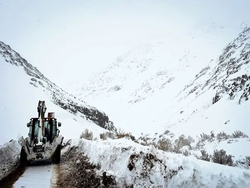 Maquinaria pesada minera detenida sobre un camino de cordillera cubierto de nieve.