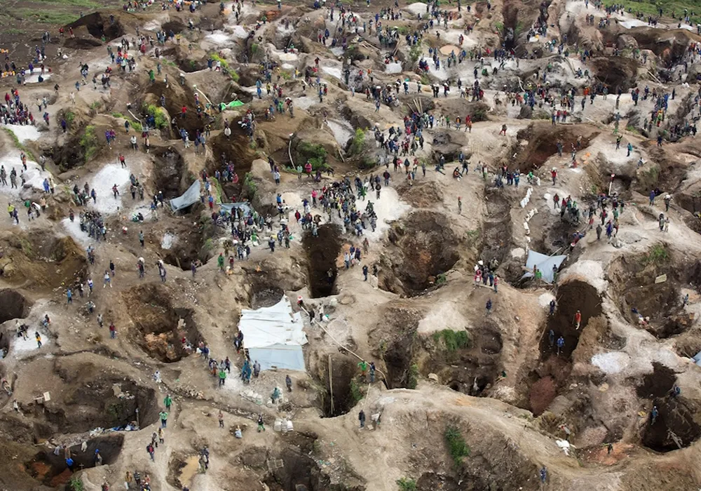 Fotografía aérea de un extenso paisaje minero que parece un cráter lunar, con miles de pozos pequeños y excavaciones que cubren todo el terreno, rodeado de vegetación en el horizonte.