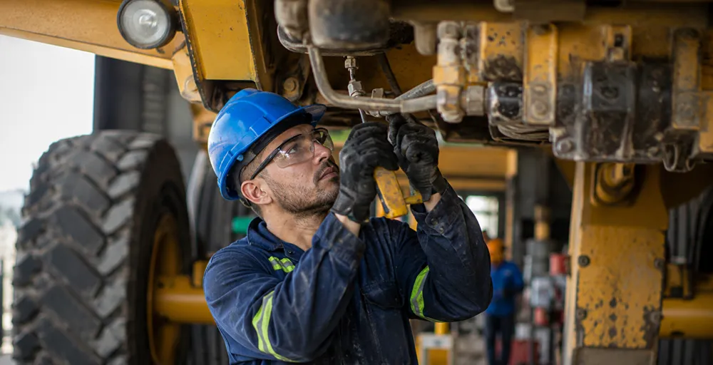 Técnico mecánico realizando tareas de mantenimiento sobre los componentes hidráulicos de un equipo pesado utilizado en operaciones mineras.