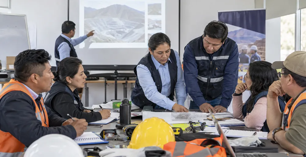 Profesionales y operarios desarrollando tareas de planificación en una obra situada entre montañas nevadas, en un contexto de logística, operación y desarrollo minero.