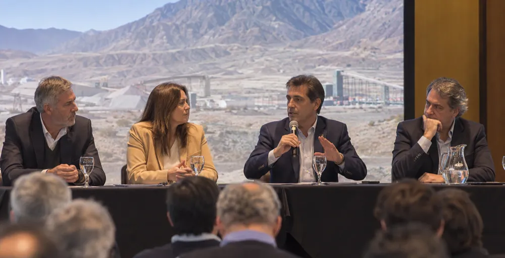 Especialistas participan de un panel profesional sobre minería, desarrollo productivo y cadena de valor, con una operación minera de montaña como contexto visual.