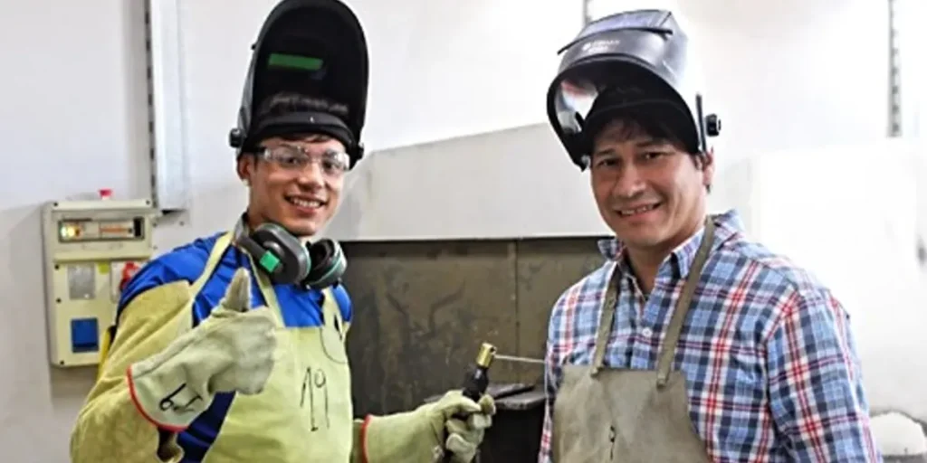 Dos participantes con máscaras, guantes y delantales de protección durante una instancia práctica de capacitación en soldadura.