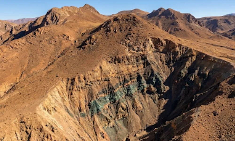 Contenido Original de ACERO Y ROCA - Prohibida su reproducción Vista hiperrealista del terreno árido cordillerano en San Juan con estratos geológicos expuestos que muestran vetas minerales en el subsuelo.
